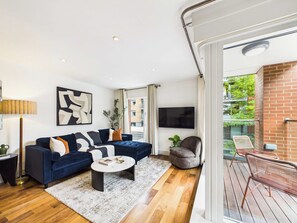 A modern living room with a sofa, coffee table, and a TV. There's a balcony with outdoor seating. - Westminster Spacious 2BR Apartment with Balcony (Greater London)