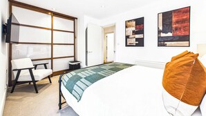 Habitación de hotel con cama, escritorio, silla, radiador y obras de arte en las paredes.