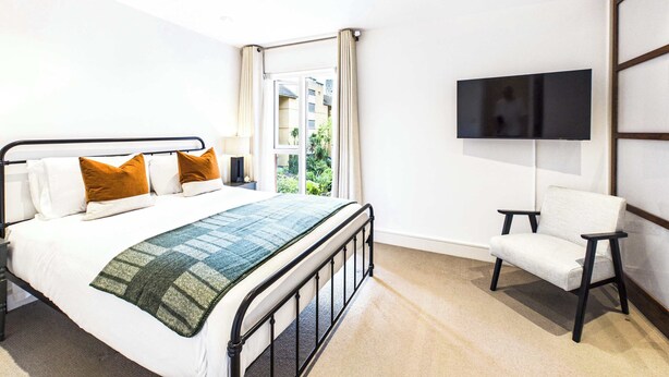 Habitación de hotel con cama, televisión, silla y ventana con vistas a zonas verdes.