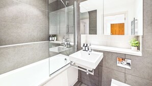 Un baño moderno con ducha envuelta en vidrio, lavamanos blanco y un espejo grande.