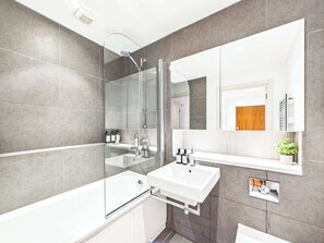 Ein modernes Badezimmer mit einer gläsernen Duschkabine, einem weißen Waschbecken und einem großen Spiegel.