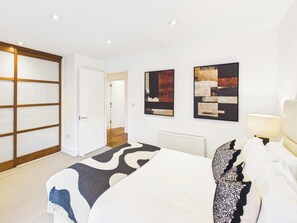 A hotel room with a bed, a nightstand, a lamp, and artwork on the wall. - Bright One Bedroom Apartment in Westminster (Greater London)