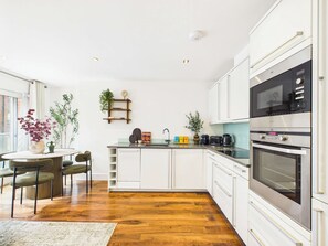 A modern kitchen with white cabinetry, a built-in oven, and a dining area with a round table and chairs. - Bright One Bedroom Apartment in Westminster (Greater London)