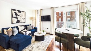 Una sala de estar moderna con un sofá azul, una mesa de centro redonda y una zona de comedor con una mesa blanca y sillas verdes.