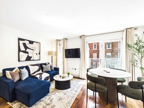 Ein modernes Wohnzimmer mit einem blauen Sofa, einem runden Couchtisch und einem Essbereich mit einem weißen Tisch und grünen Stühlen.