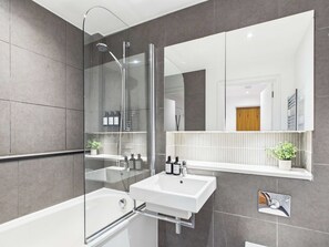 A modern bathroom with a glass-enclosed shower, a white sink, and a mirror above the sink. - Bright One Bedroom Apartment in Westminster (Greater London)