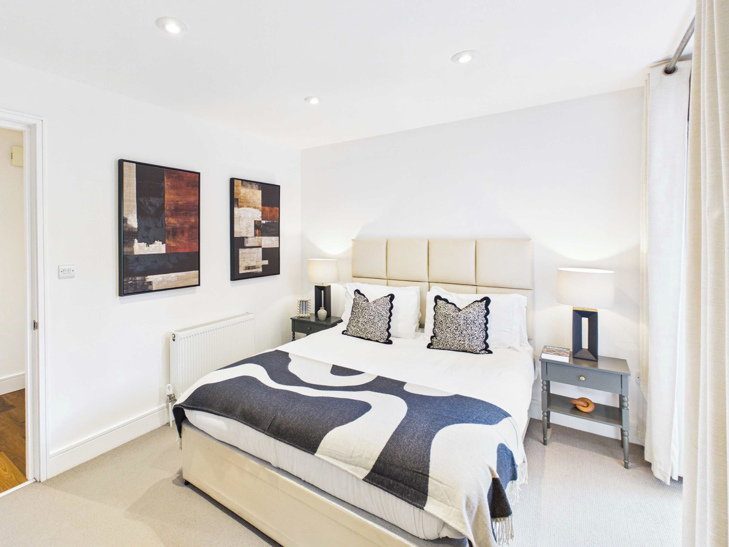A bedroom with a bed, two bedside tables, a radiator, and artwork on the wall.