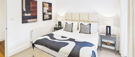A bedroom with a bed, two bedside tables, a radiator, and artwork on the wall.