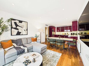 Ein stilvolles Wohnzimmer mit einem grauen Sofa, einem Couchtisch mit Dekoration und einem großen, abstrakten Gemälde an der Wand.