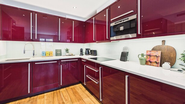 A modern kitchen with red cabinets, a stainless steel range hood, and a white countertop. - Spacious and Bright Westminster Apartment (Greater London)