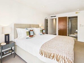 Une chambre d’hôtel comprenant un lit, une table de chevet, une lampe et une porte donnant accès à une salle de bain.