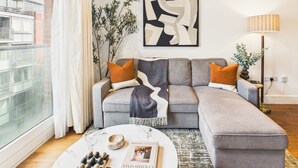 A modern living room with a grey sectional sofa, a round coffee table, and a large abstract painting. - Spacious and Bright Westminster Apartment (Greater London)