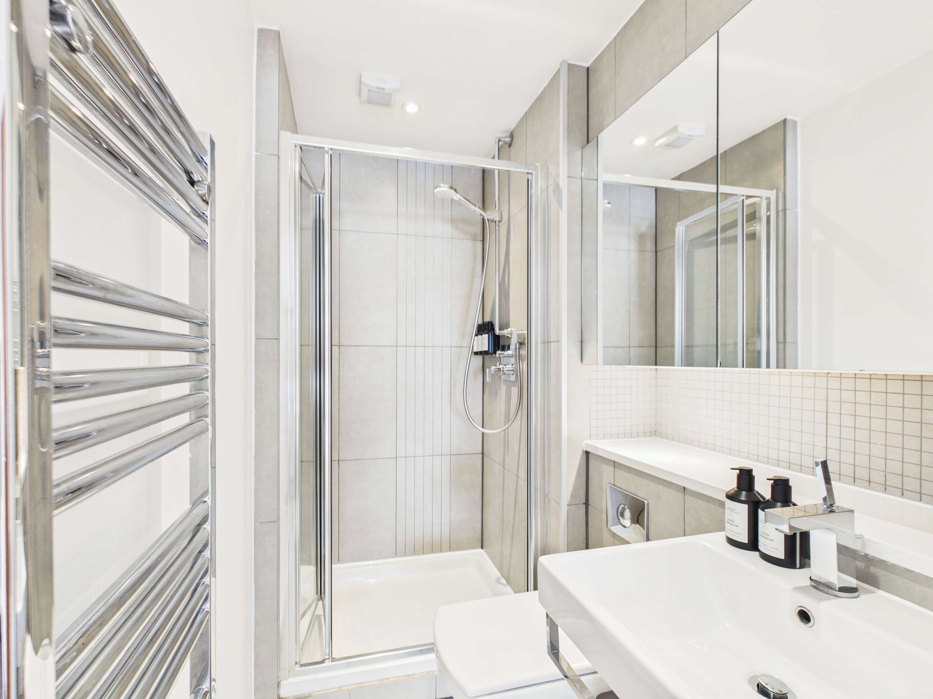 Un baño moderno con cabina de ducha de vidrio, un lavabo blanco y un espejo grande.