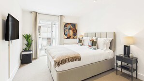 A hotel room with a large bed, a flat-screen TV, a potted plant, and a painting on the wall. - Spacious and Bright Westminster Apartment (Greater London)