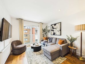 A modern living room with a sofa, armchair, coffee table, and floor lamp. - Spacious and Bright Westminster Apartment (Greater London)