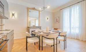 A dining room with a round table, white chairs, a fireplace, and a large mirror. - COMBINING AN UNBEATABLE LOCATION WITH MODERN COMFORTS – SAINT GERMAIN (Paris)