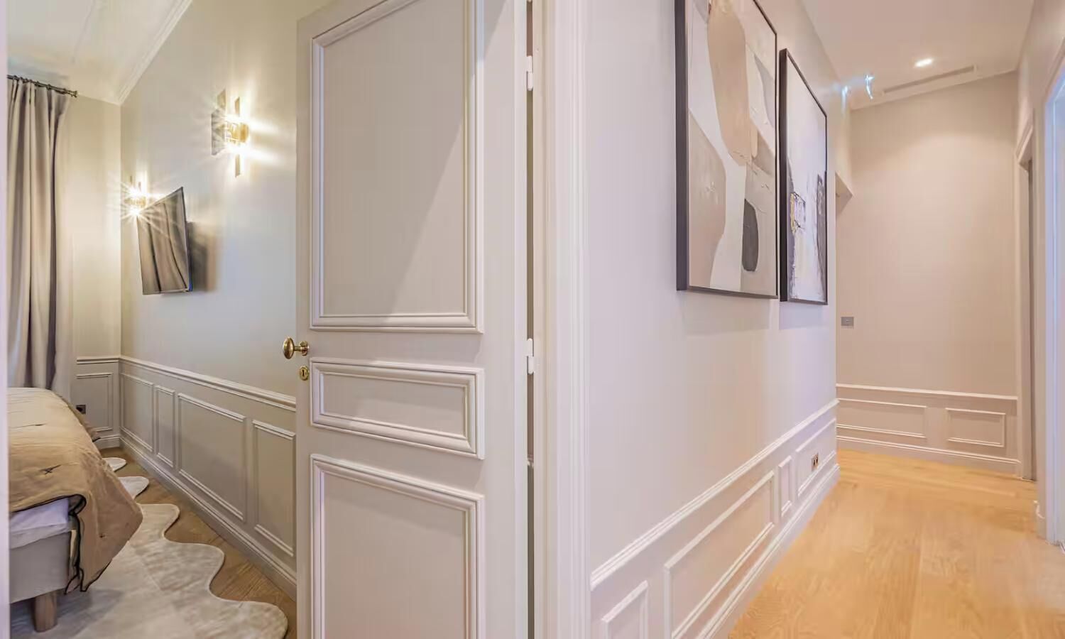 Un couloir avec une porte, un lit et un luminaire fixé au mur.
