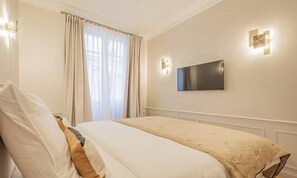 A hotel room with a bed, a TV mounted on the wall, and a window with curtains. - COMBINING AN UNBEATABLE LOCATION WITH MODERN COMFORTS – SAINT GERMAIN (Paris)
