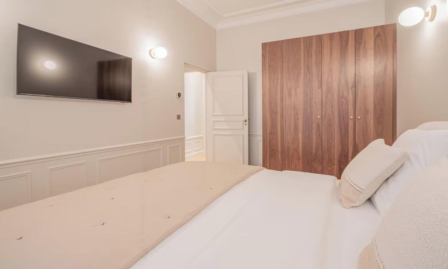 Een slaapkamer met een bed, een kledingkast, een aan de muur bevestigde televisie en een deur naar een andere kamer.
