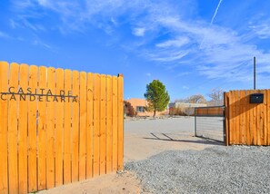 Una porta de fusta amb la inscripció 'CASITA DE CANDEJARITA', que condueix a una zona d'aparcament amb sòl de grava i un edifici al fons.