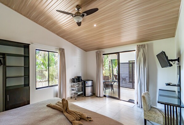 A hotel room with a bed, a desk, a chair, a television, and a balcony with a view of greenery.