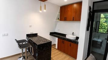 Una cocina moderna con una isla central, taburetes de bar, armarios de madera y un baño con paredes de vidrio.