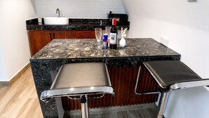A compact kitchen with a marble countertop, wooden cabinets, a sink, and a bar area with stools. - EVERGREEN VILLA (Dar es Salaam)