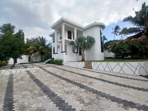 A two-story building with a symmetrical facade, a central entrance, and a paved courtyard with geometric patterns. - EVERGREEN VILLA (Dar es Salaam)