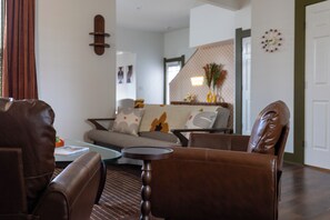 A living room with a brown leather sofa, a glass coffee table, and a patterned rug. - Walk to Mass Ave , Charming 3BR with 2 Kings, Garage & fire pit (Indianapolis)