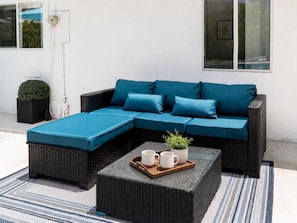 Ein modulares Sofa mit blauen Kissen, ein passender Hocker und ein Tablett mit Tassen und einer Pflanze.