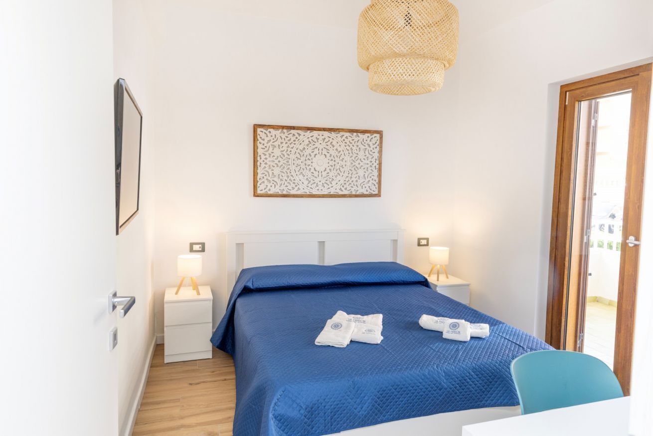 A hotel room with a bed, bedside tables, a hanging light fixture, and a door.