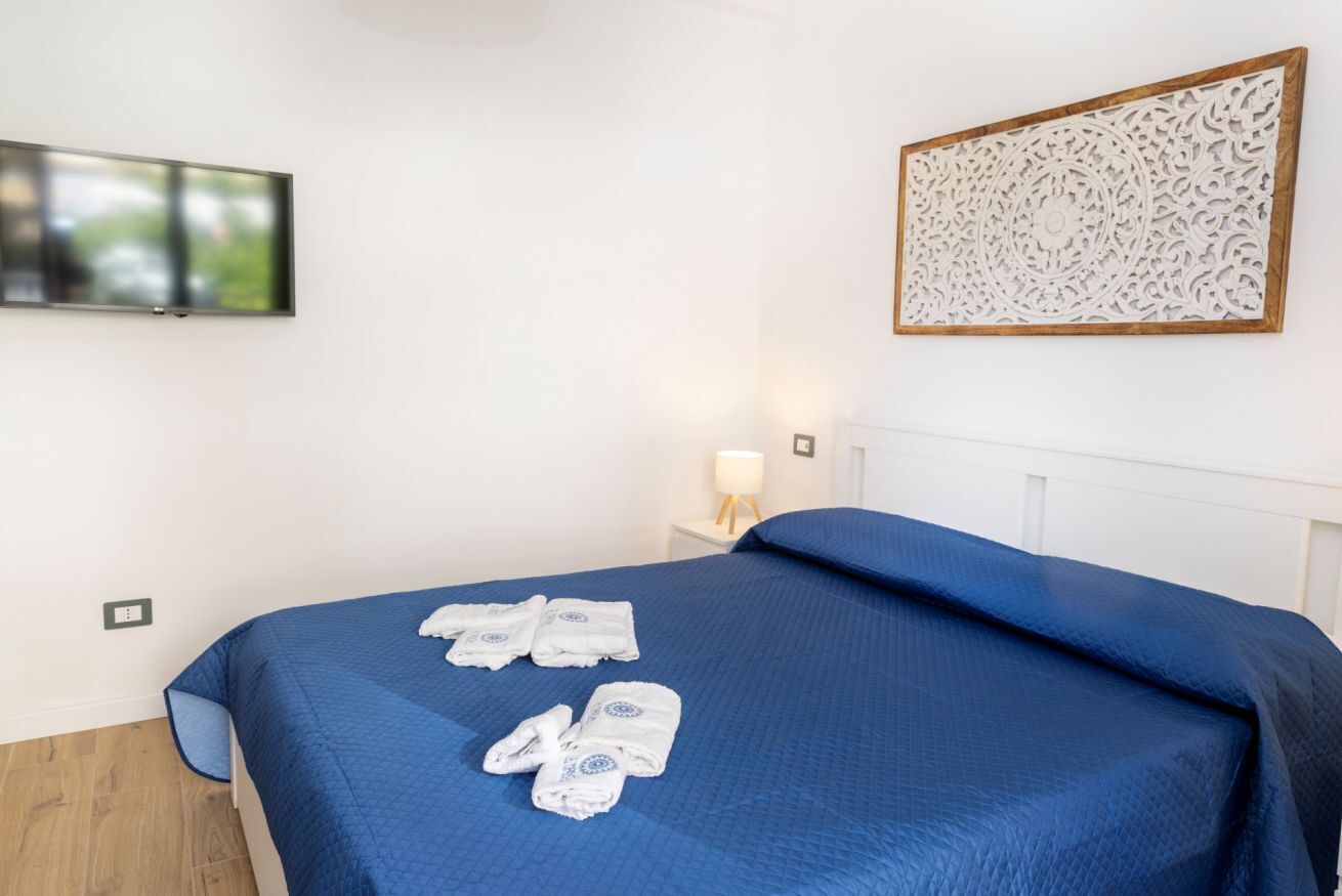 A hotel room with a bed, a television mounted on the wall, and a decorative panel above the bed.