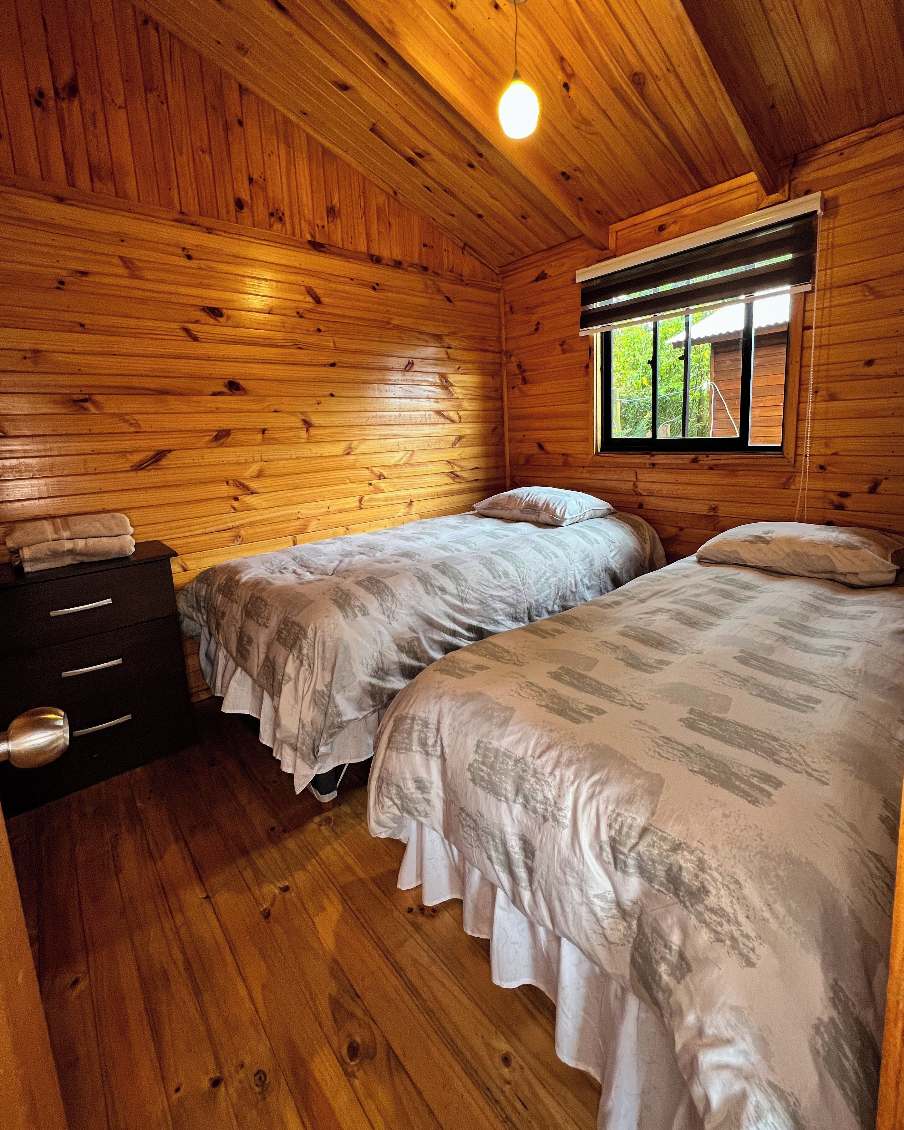 A wooden cabin bedroom with two beds, a dresser, and a window.