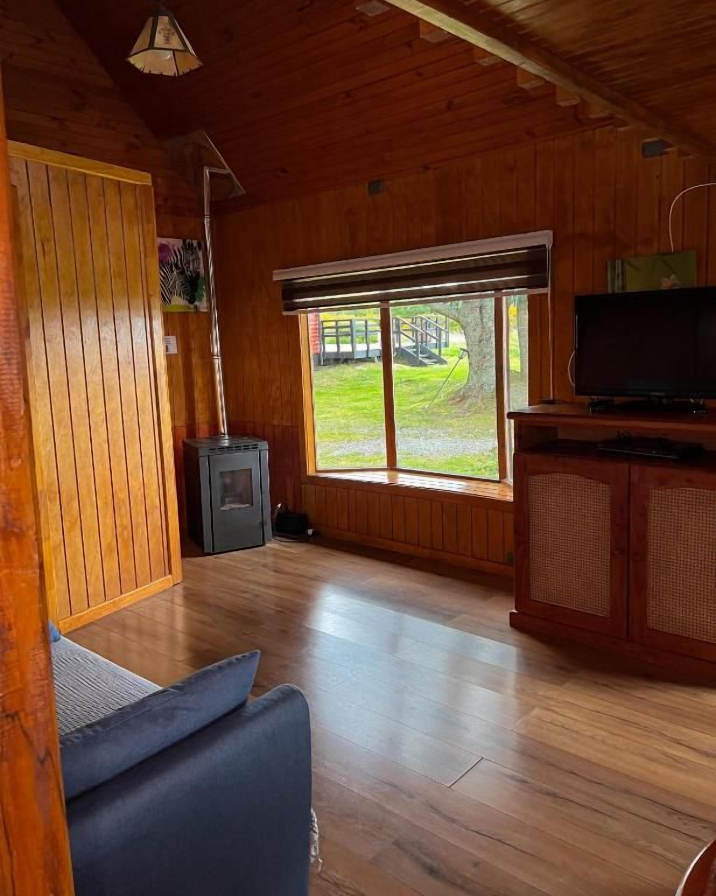 Un interior de madera con un sofá, un televisor y un ventanal grande.