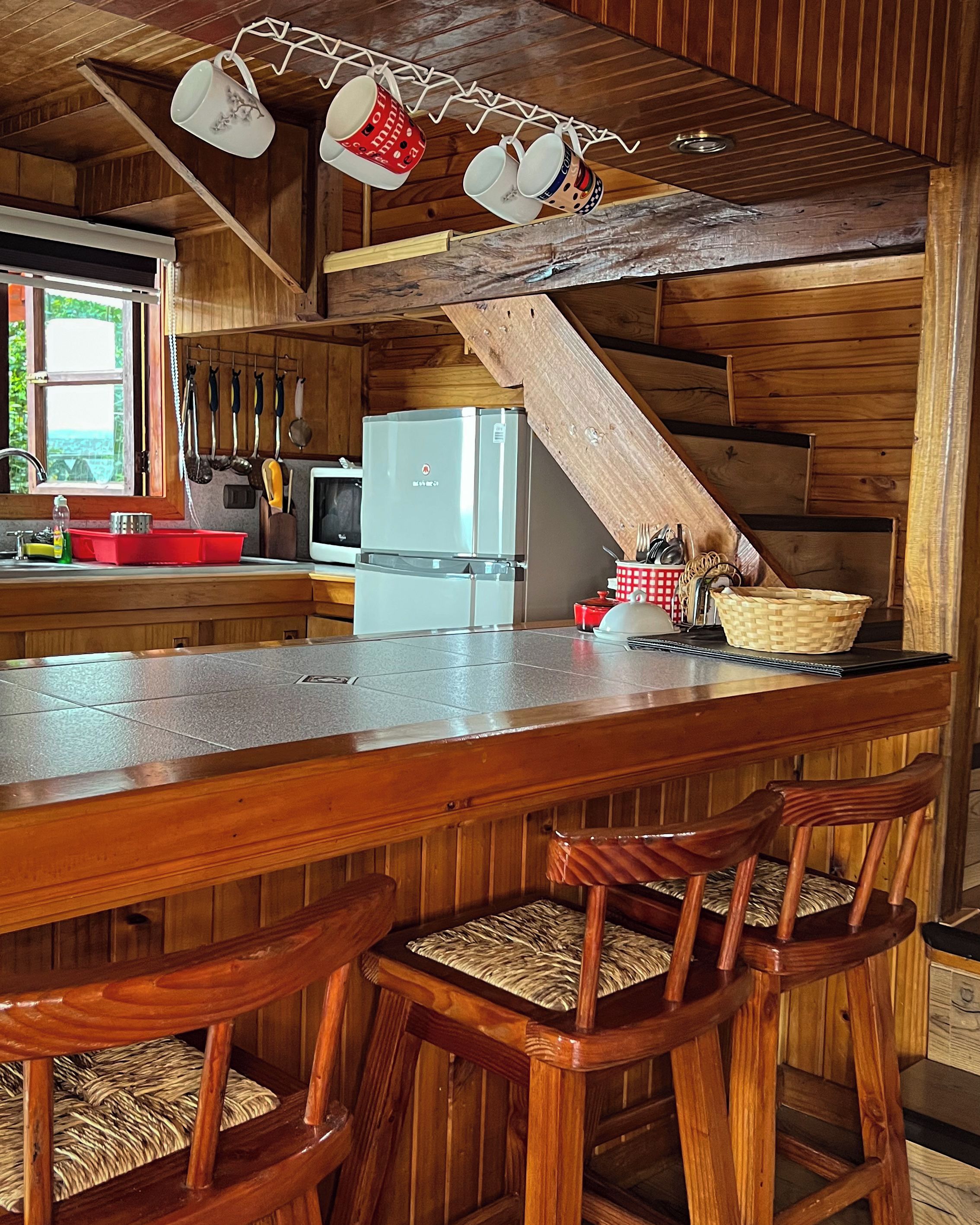 Una cocina rústica con paredes de madera, una zona de bar con taburetes y tazas colgando.