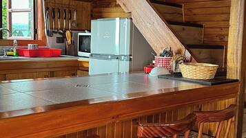 Una cocina rústica con paredes de madera, una zona de bar con taburetes y tazas colgando.