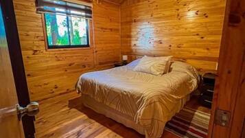 A wooden cabin bedroom with a bed, a window, and a door.