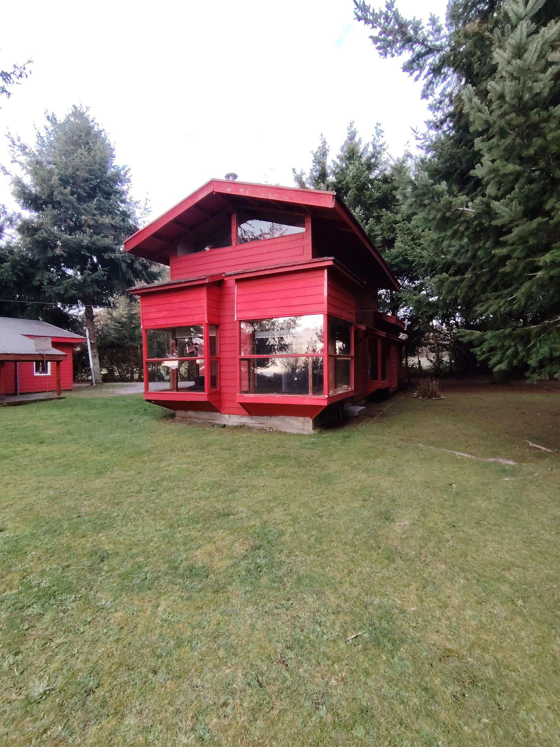 A red two-story building with large windows and a flat roof, surrounded by grass and trees.