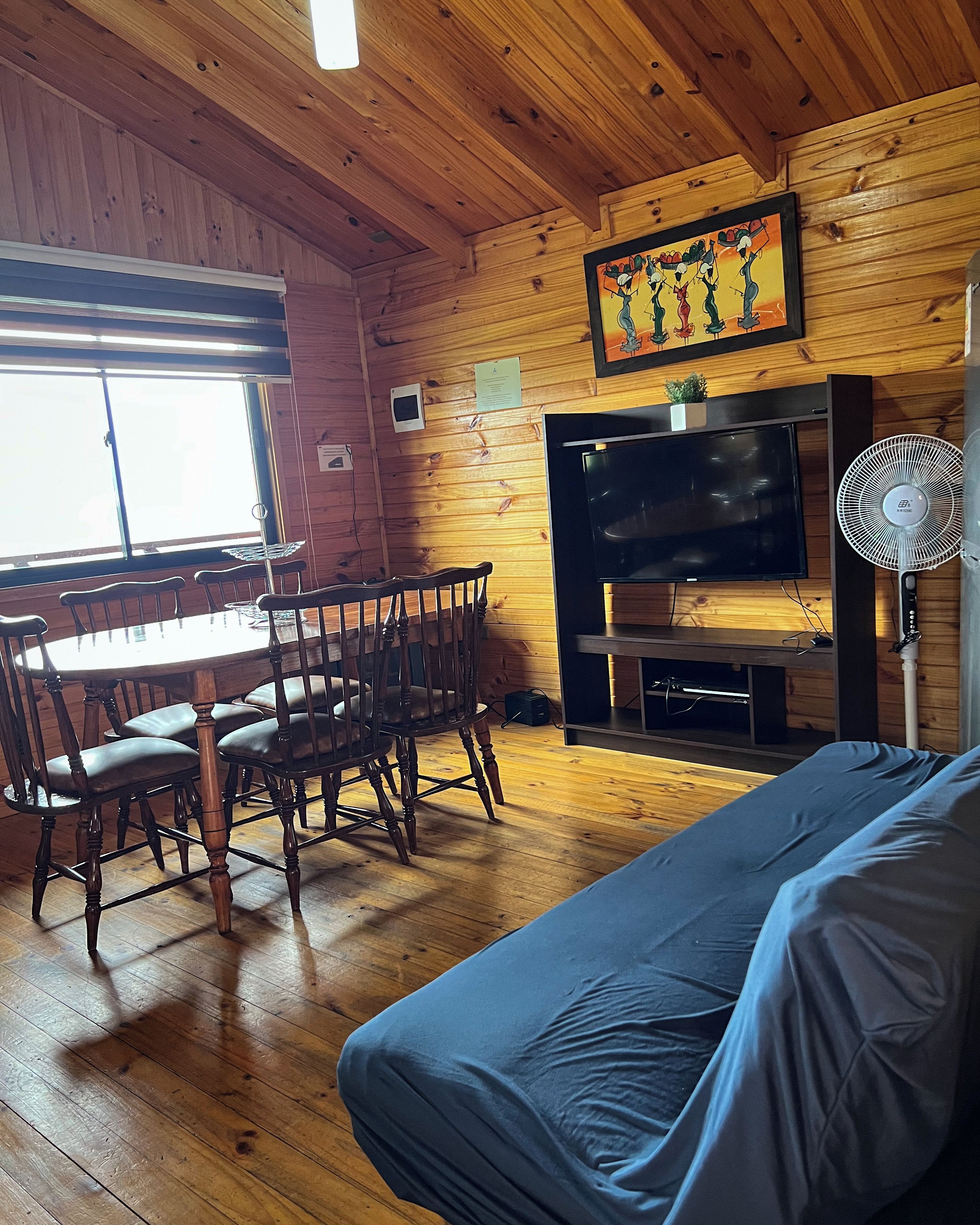 Un interior de madera con una mesa de comedor, sillas, un sofá, un televisor y un ventilador.