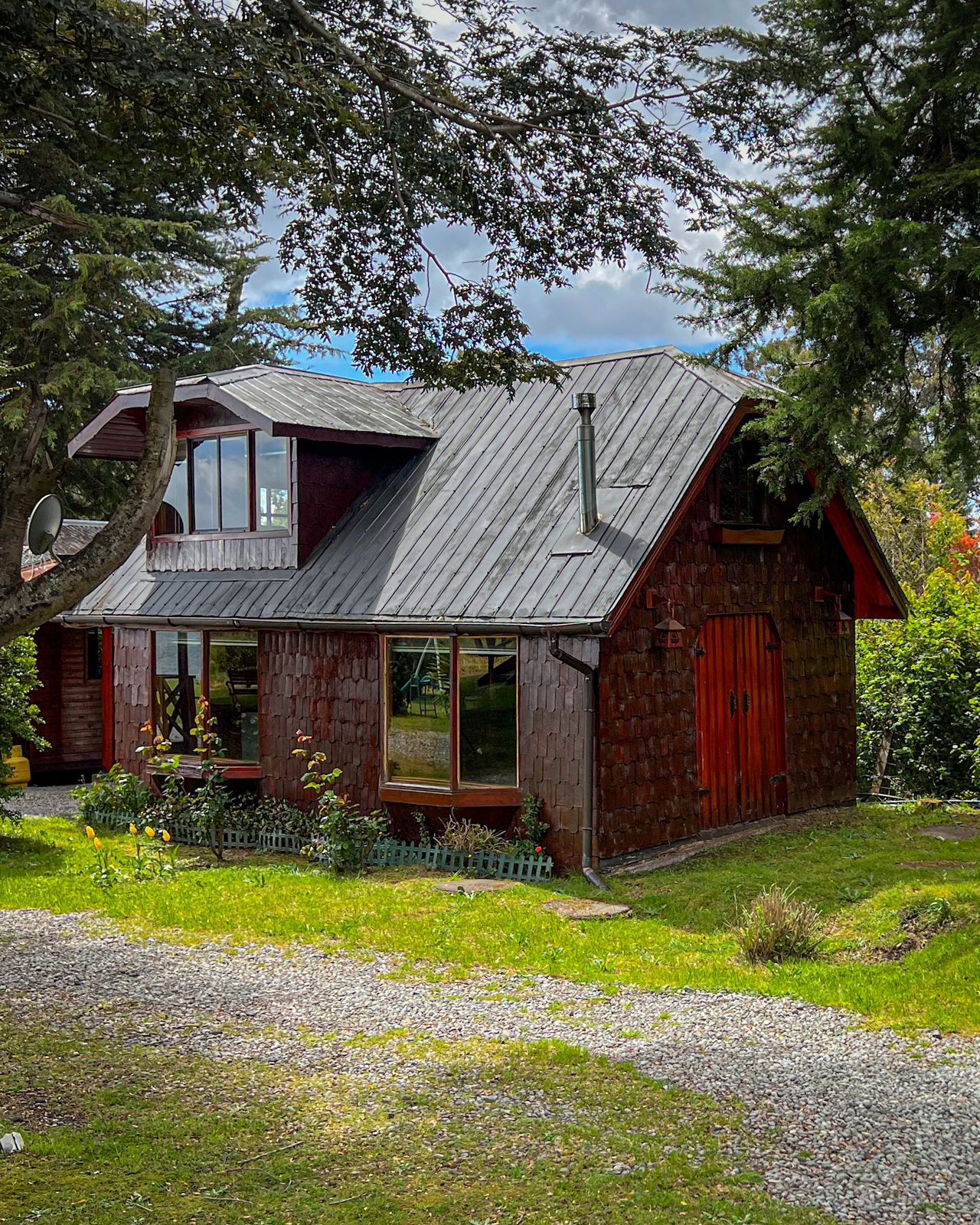 Ett rustikt trähus med ett sluttande tak, en synlig skorsten och en veranda med en bänk.
