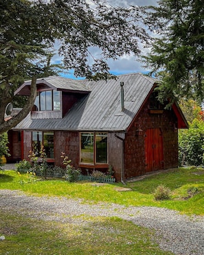 Ett rustikt trähus med ett sluttande tak, en synlig skorsten och en veranda med en bänk.