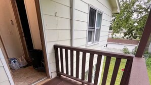 Una terraza de madera con barandilla, una puerta que da a un espacio interior y un ventanal.