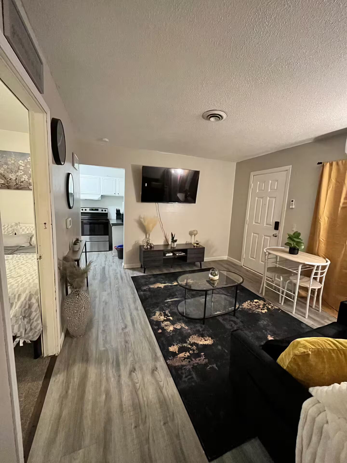 Un salon moderne avec un long plancher en bois, un tapis à motifs noir et blanc, une table basse en verre et un canapé blanc.