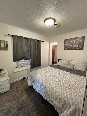 A bedroom with a bed, curtains, a painting, and a radiator. - Cozy Apartment near Highland Park (Des Moines)