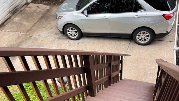 Una escalera de madera que lleva a un garaje donde se estaciona una camioneta SUV plateada.