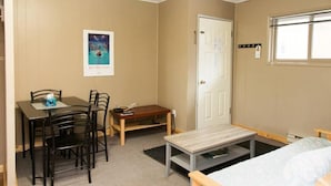 A room with a bed, a desk with chairs, a small table, and a poster on the wall. - Lone Star Motel (Rossland)