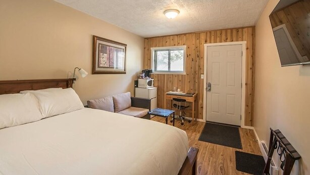 A bedroom with a bed, a desk, a chair, a microwave, and a door. - Lone Star Motel (Rossland)