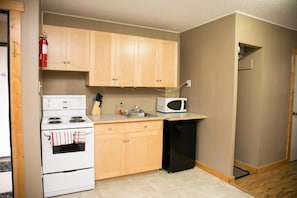 A compact kitchen with wooden cabinets, a white stove, a black refrigerator, and a microwave.