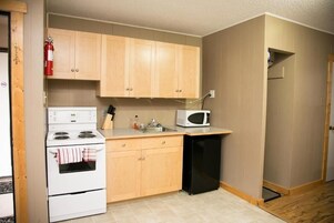 Una cocina compacta con armarios de madera, estufa blanca, refrigerador negro y microondas.