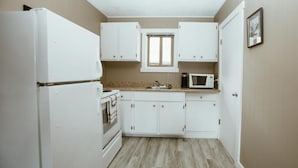 A compact kitchen with white cabinets, a built-in oven, a microwave, and a window above the sink. - Lone Star Motel (Rossland)